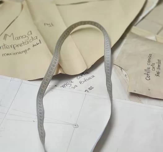 Patrones de papel con anotaciones y una cinta métrica sobre la mesa de corte
