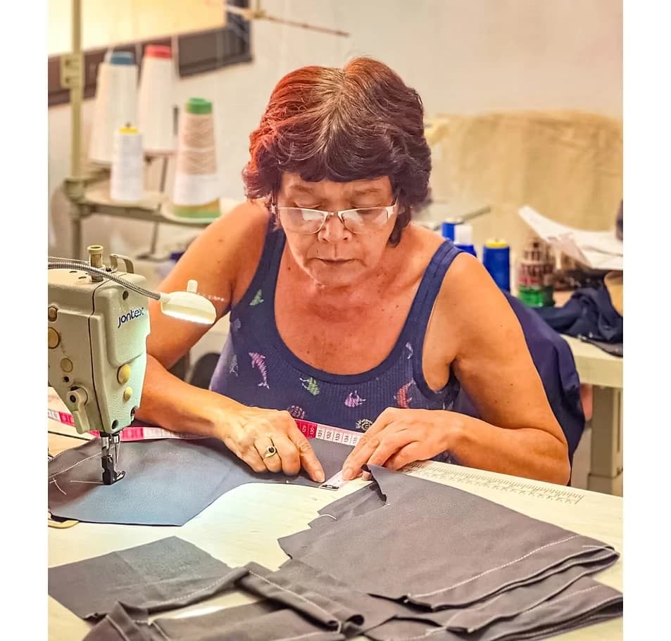 Costurera con gafas cortando telas oscuras junto a su máquina de coser