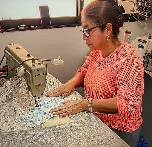 Costurera con gafas y blusa coral cosiendo una tela blanca estampada en su máquina