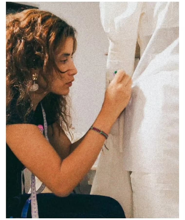 Diseñadora de cabello rizado ajustando una tela sobre un maniquí en el taller