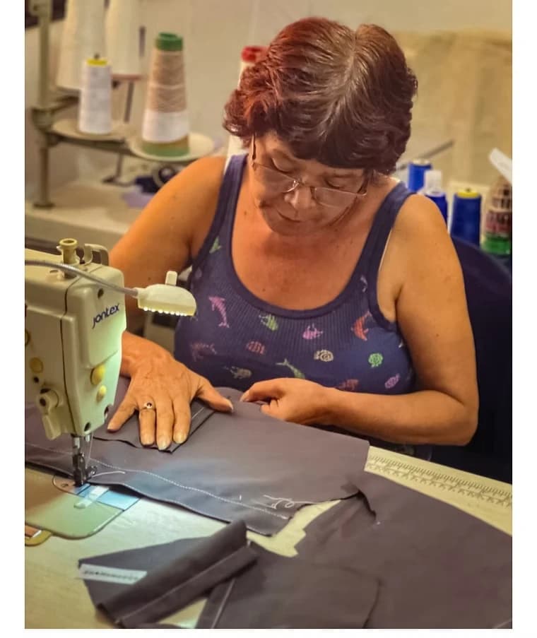 Costurera con gafas cortando tela oscura junto a su máquina de coser